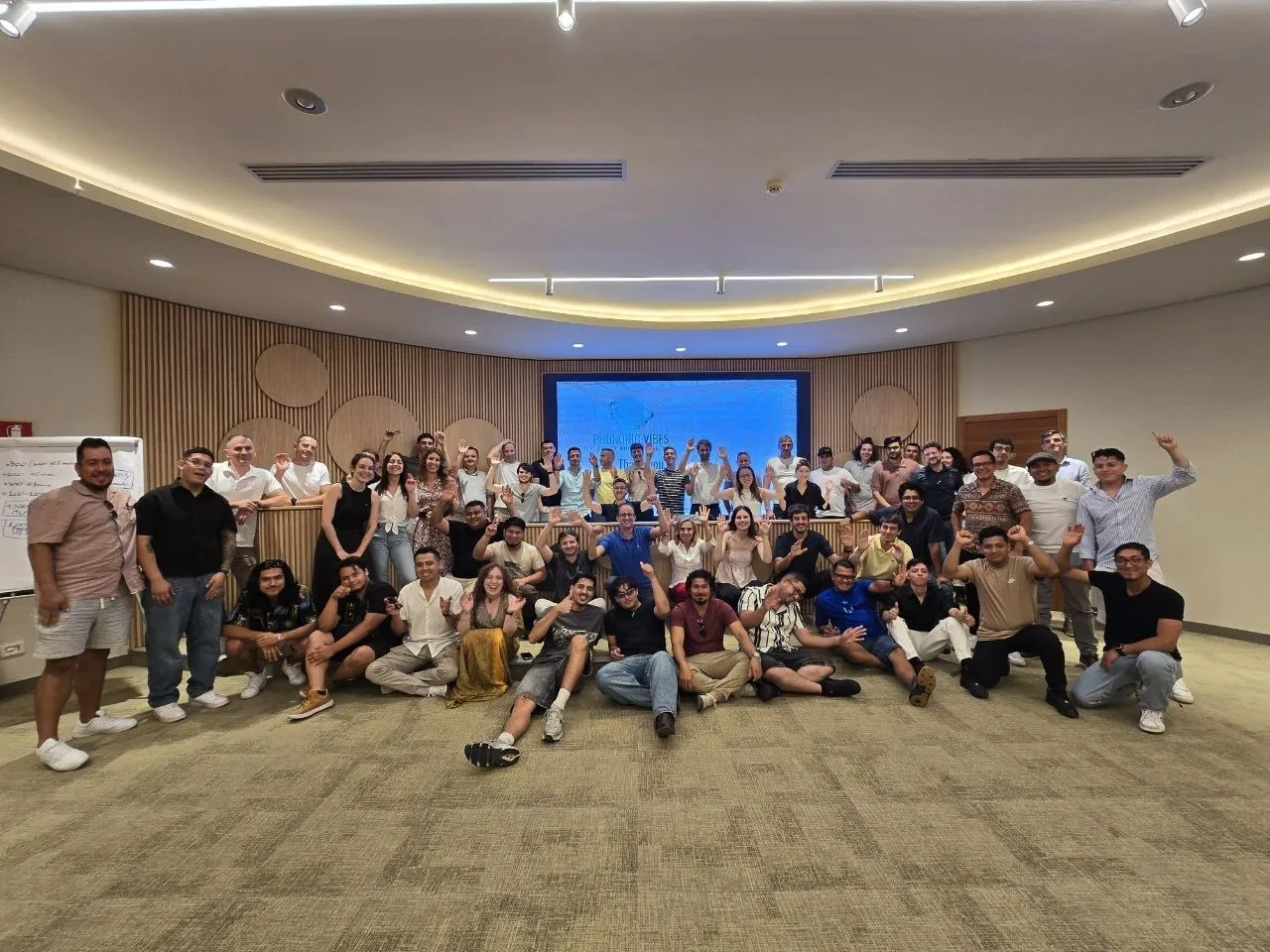 The Phononic Vibes team, about sixty people, waving and sitting together in a conference room in front of a screen showing the Phononic Vibes name