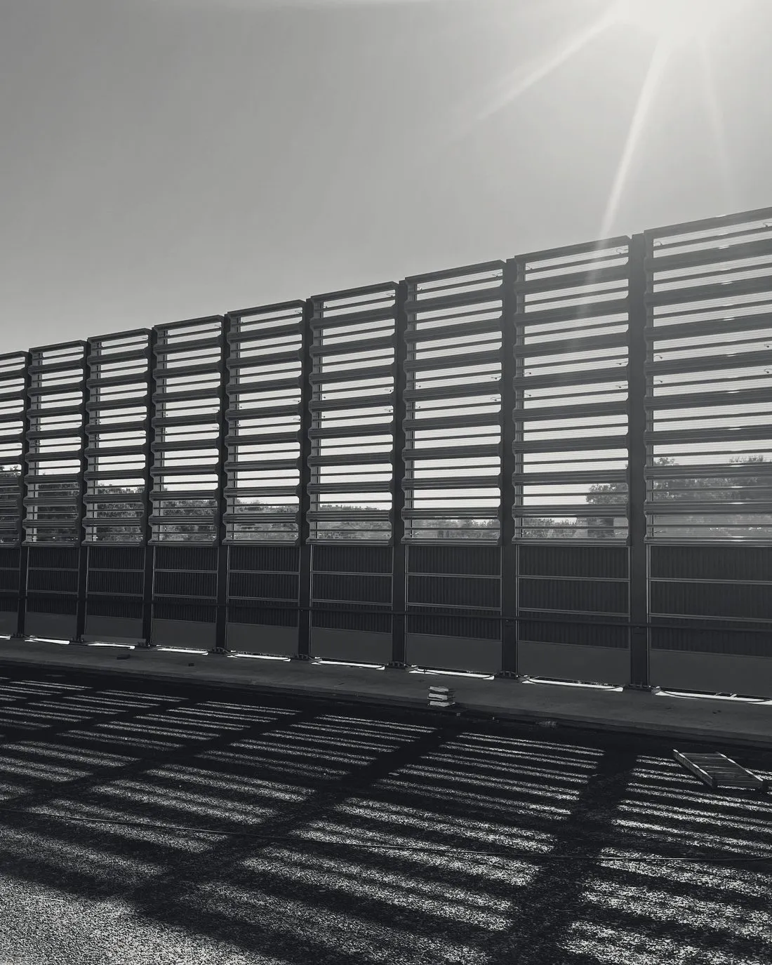 Sun through MetaWindow slats casting a lattice of shadow across the road deck